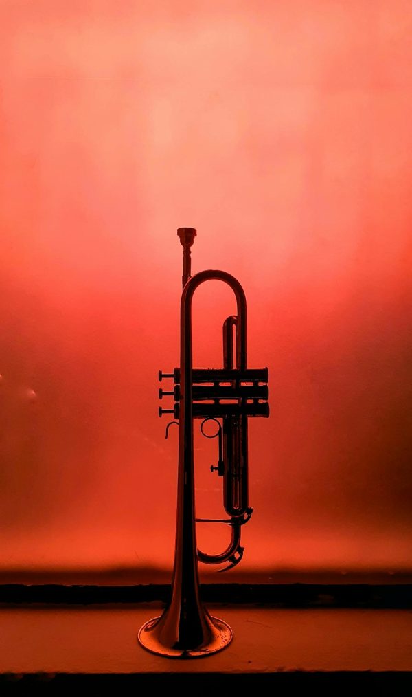 A single trumpet stands silhouetted against a vivid orange background, creating a dramatic musical image.