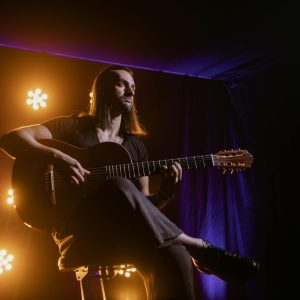 Musician playing guitar under dramatic stage lighting in a club setting.