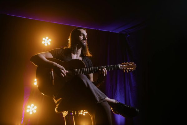 Musician playing guitar under dramatic stage lighting in a club setting.