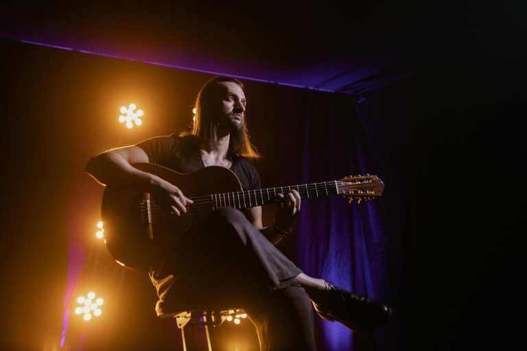 Musician playing guitar under dramatic stage lighting in a club setting.